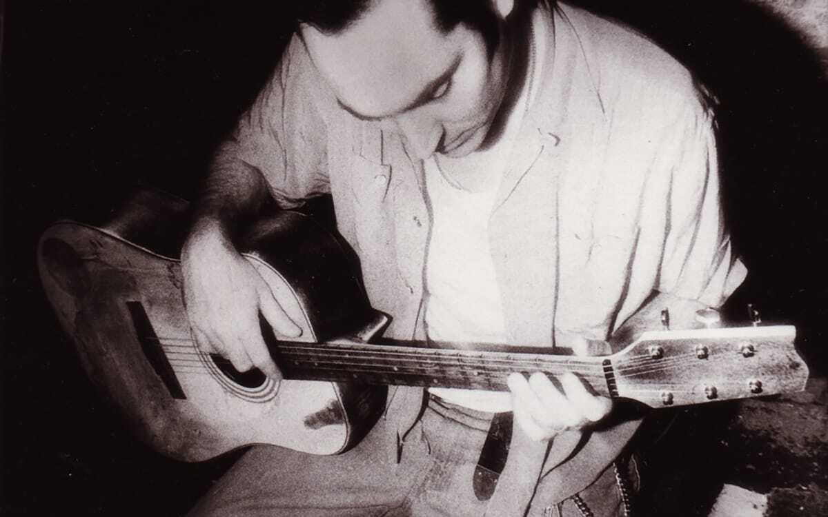A black-and-white photo of Michael Knott staring down at an acoustic guitar