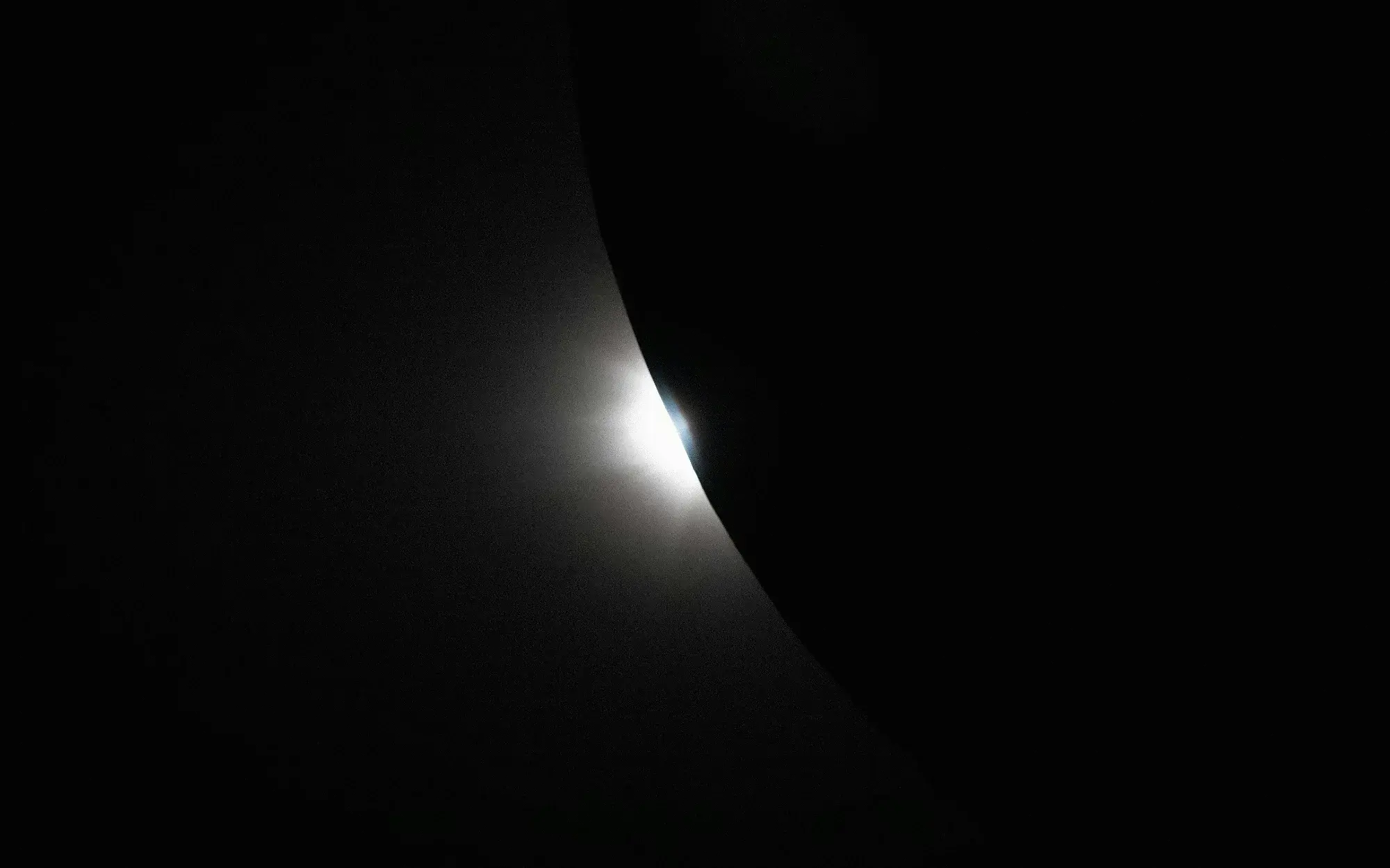 A stark black-and-white image of the Sun peeking out from behind the moon
