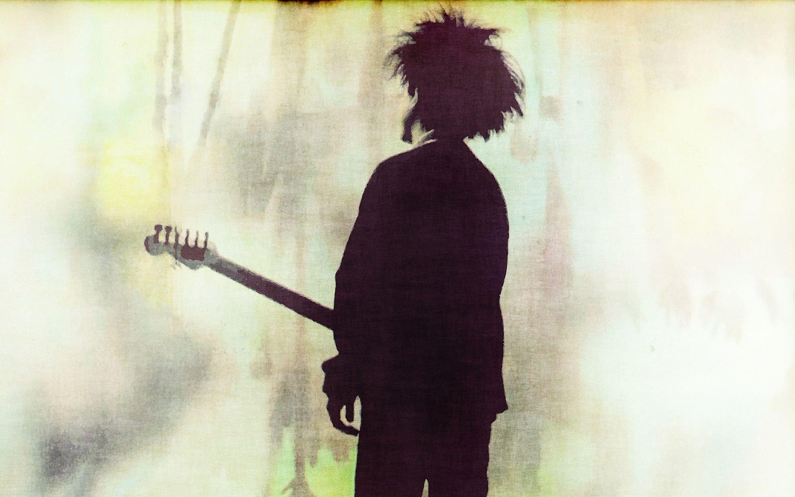Robert Smith of The Cure, holding a guitar, with his back turned to us