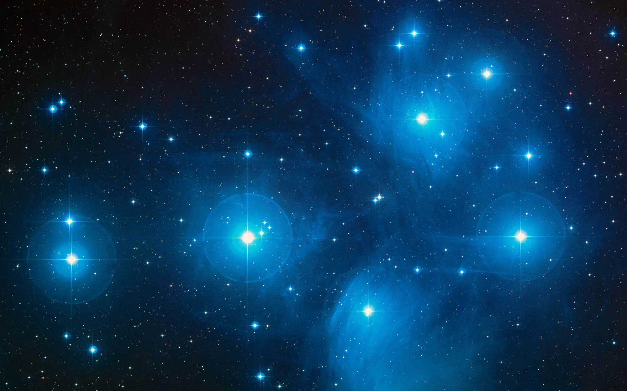 A photo of the Pleiades star cluster depicting an array of blue-white stars shimmering in space