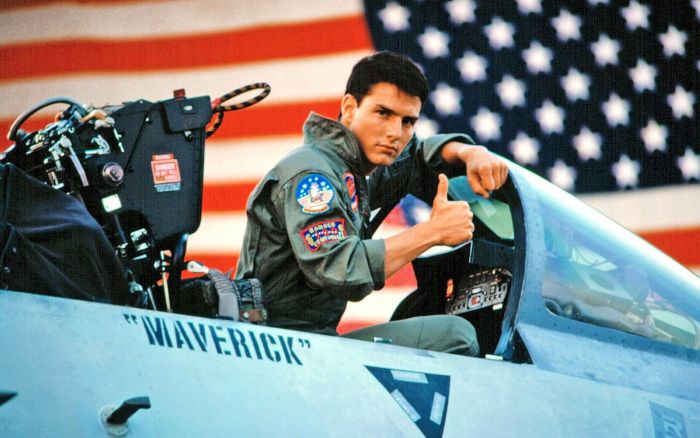 Tom Cruise giving a thumbs up while sitting in an F-14 Tomcat, with an American flag behind him